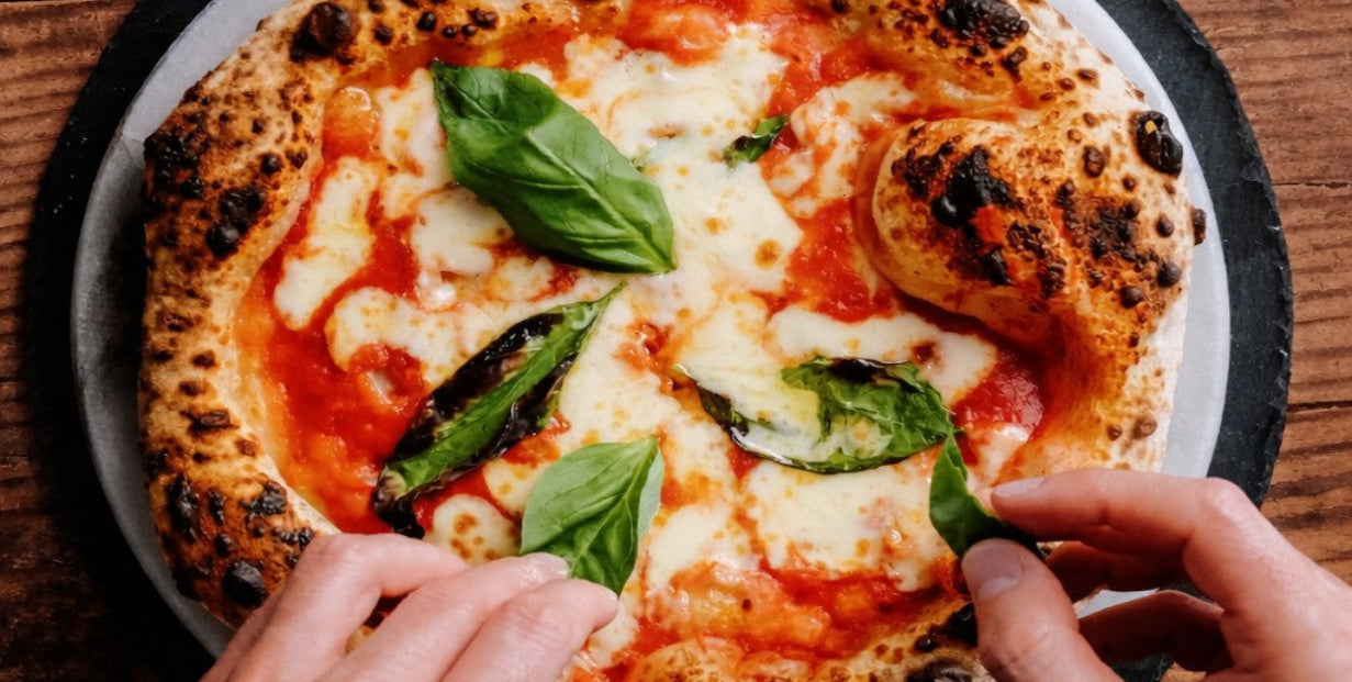 Person adding basil leaves to a pizza on a wooden table
